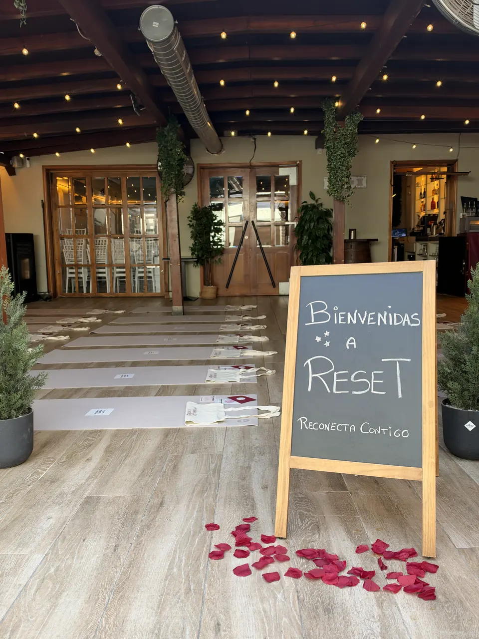 Pizarra con el mensaje «Bienvenidas a Reset. Reconecta Contigo» y pétalos de rosa en la entrada de la sala